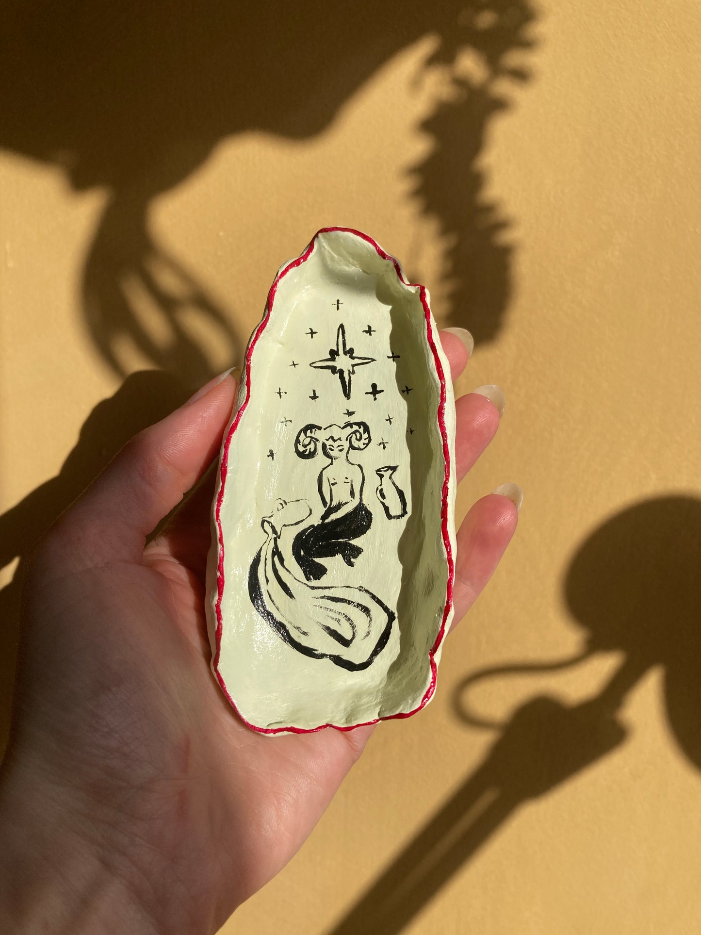 Hand holding a small decorative dish with satyr and spilt vessel under stars design on an off white background